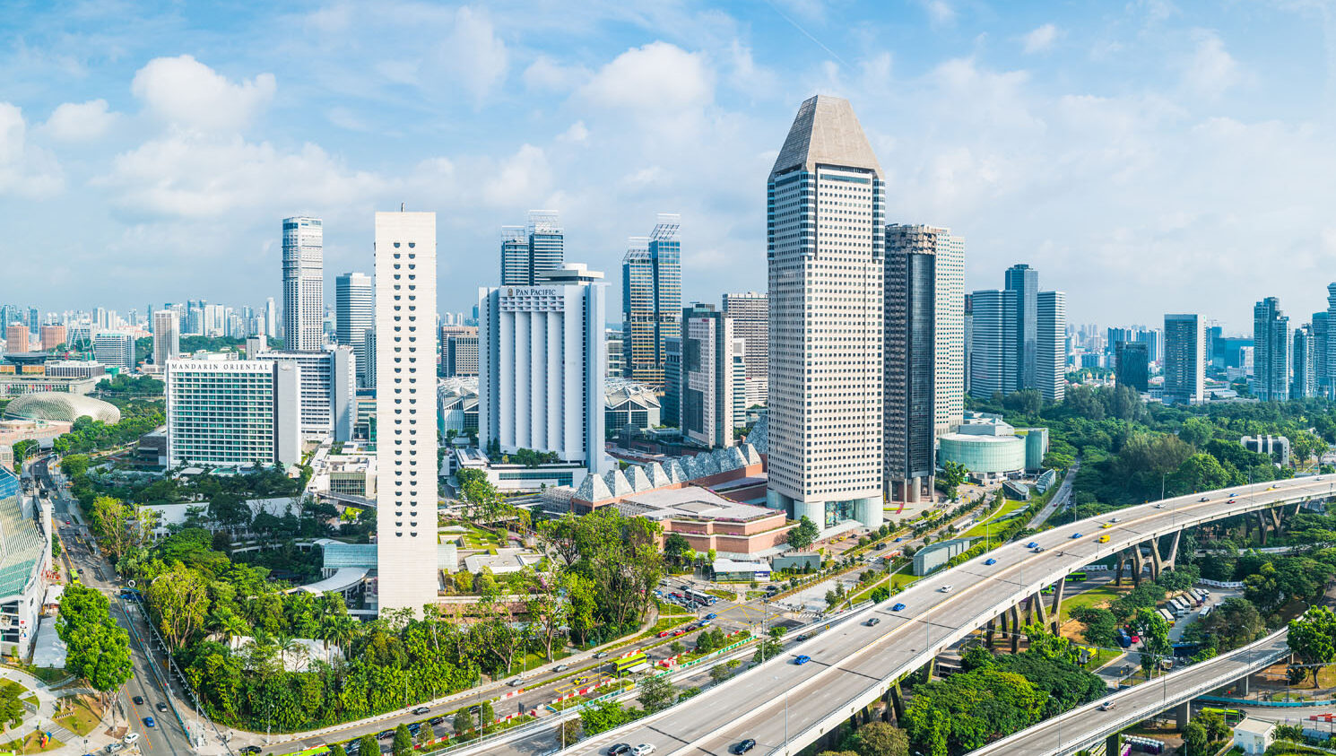 Aerial panorama over the towering skyscrapers and busy highways of downtown Singapore surrounding Marina Bay.